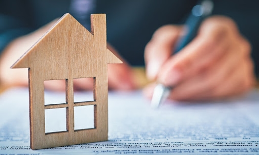 wooden house in front of a man signing with a pen